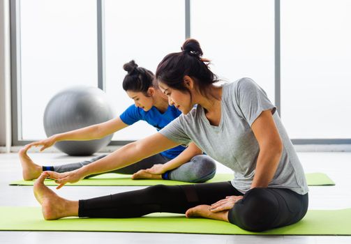 Two Asian women sporty attractive people practicing yoga lesson together, working out at the fitness GYM, Young and senior female exercising do yoga in yoga classes, sport healthy lifestyle