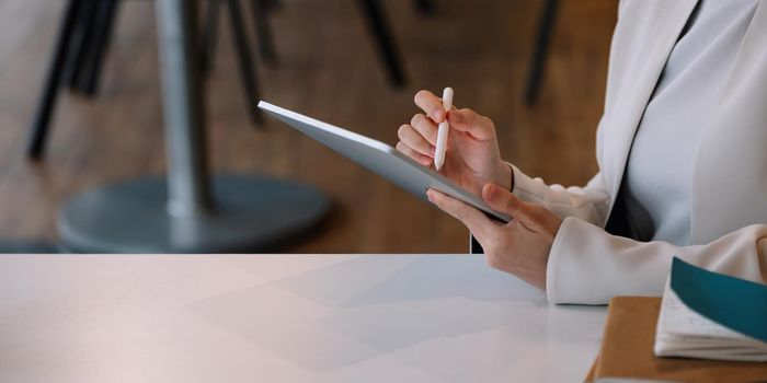 Close up businesswoman holds pen stylus drawing on digital tablet on workplace.