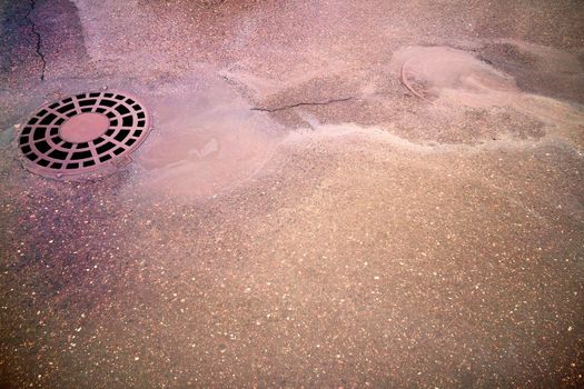 Oil slick on the asphalt road background drains into the storm drain. Water pollution environmental problems