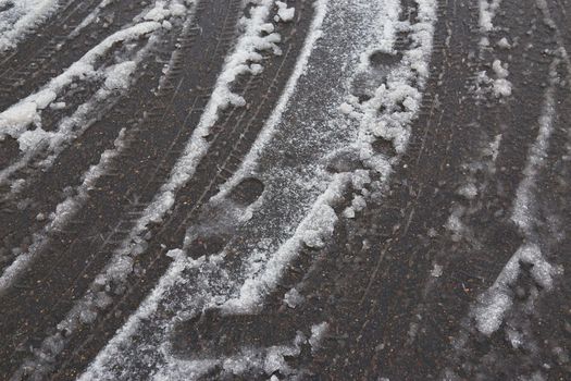 Tire tracks in the melting snow on asphalt road