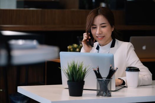 Portrait of young woman smiling cheerful entrepreneur in office making phone call while working with laptop