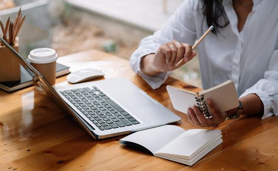 Cropped photo of woman writing making list taking notes in notepad working or learning on laptop indoors- educational course or training, seminar, education online concept