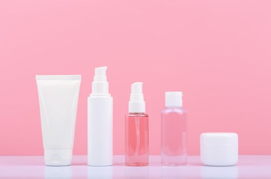Set of cosmetic products in tubes in a row on white table against bright pink background. Concept of daily skin care routine for anti aging, regular or anti acne treatment