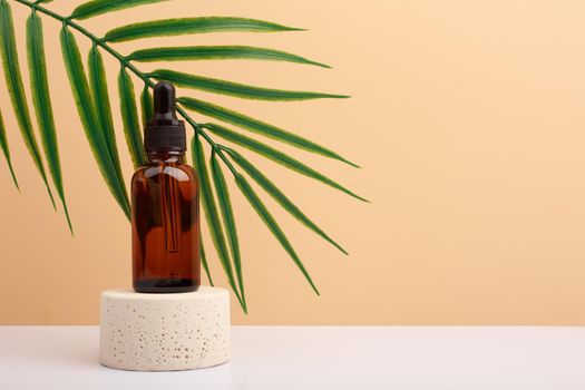 Skin serum on beige stone podium with palm leaf on white table against beige background with copy space. 