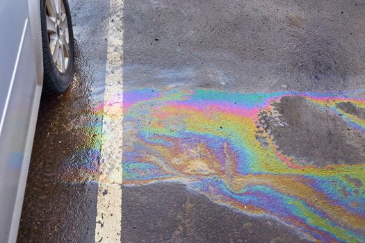 Colorful gas stain on wet asphalt. Oil stain or gasoline caused by a leak under a car. Environmental pollution concept.