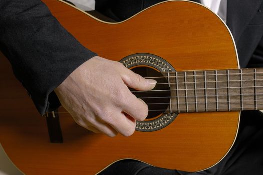 A man sitting and playing classic wooden guitar close up