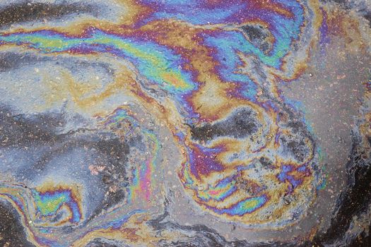 A circular rainbow gasoline stain on the asphalt. Image with noise effect.
