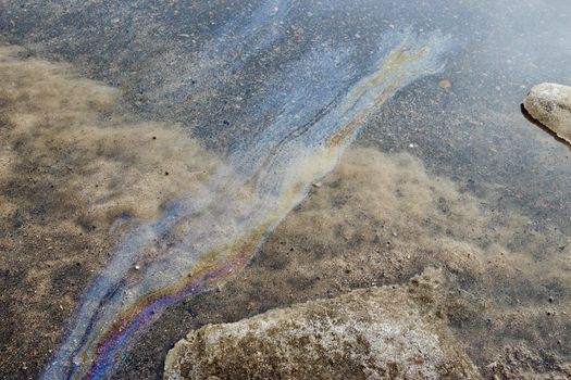 Rainbow gasoline stain on the asphalt. Snow melts after winter