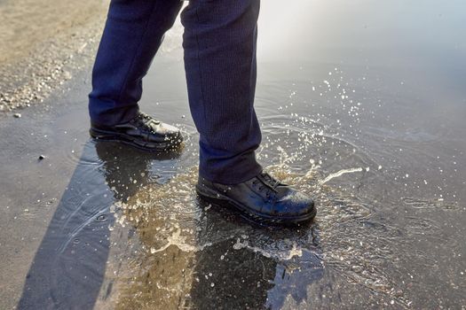 Male feet in shoes walk on a puddle of melted snow. Selective focus