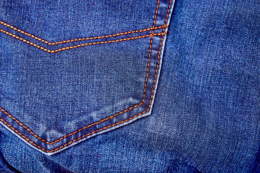 Blue denim jeans background pocket with seam and orange thread stitches close-up. Casual urban classic fashion