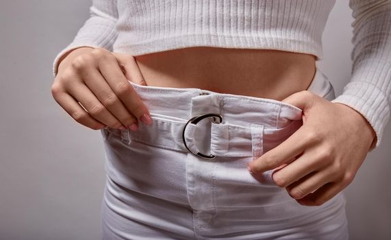 woman holding hands on the belt of light trousers