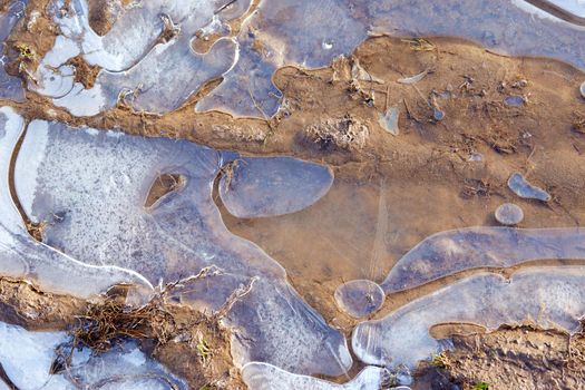 The surface of frozen water in a small puddle, snow and sand lie on top.Closeup.Air frozen in ice creates white bubbles. The first autumn frosts.