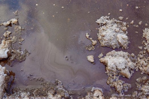 Rainbow stains from gasoline and oil on the asphalt surface in winter.
