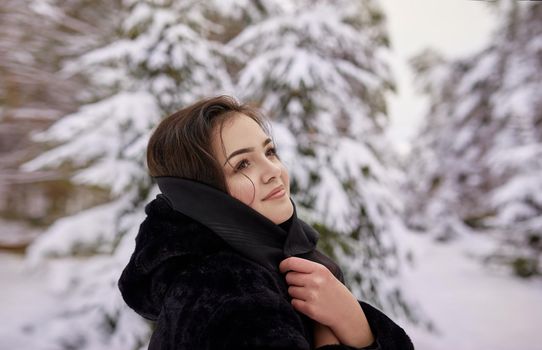 close up winter portrait of dreamy young woman walking in snowy forest with trees on background