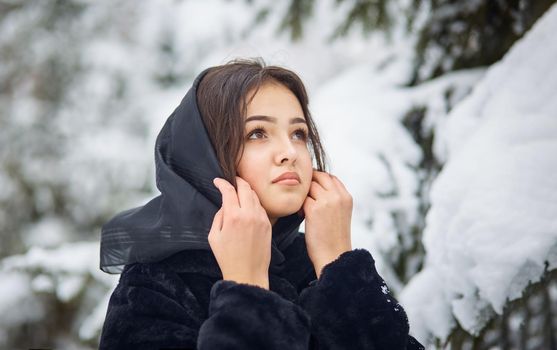 close up winter portrait of dreamy young woman walking in snowy forest with trees on background