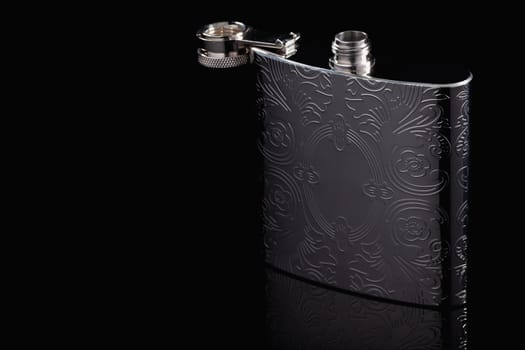 Stainless hip flask on the black glass table. Flask for alcohol. Lifestyle and travel.