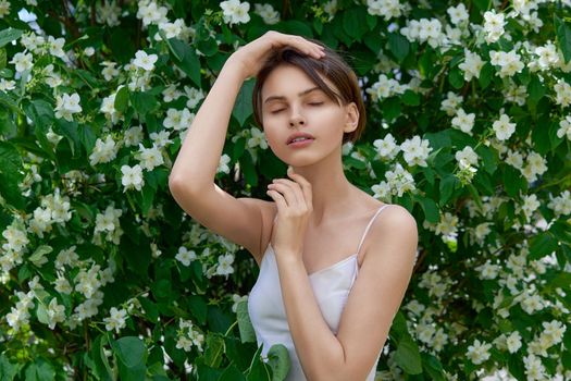 Attractive modest young woman natural makeup in a white dress outdoors against the background of blooming jasmine