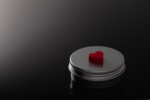 Silver metal containers for cosmetics and a red heart isolated on the black glass desk.
