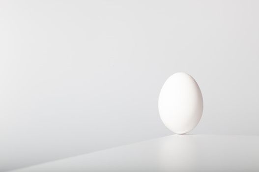 White egg balances on the edge of the white table.