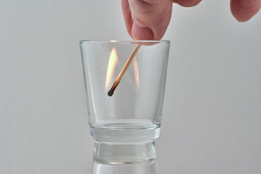 Hand holds a burning match in a transparent glass. Close up