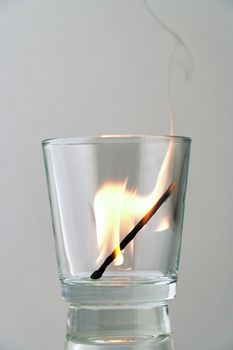 Burning match in a transparent glass on a light background. Concept, symbol