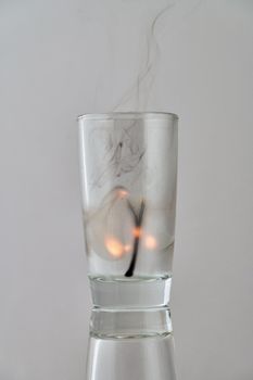 Remains of a dying match in a transparent glass on a light background. Concept, symbol