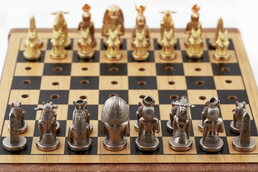 Chess board with placed chess pieces stylized as Egyptian gods. Focus on silver pieces