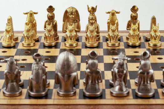 Chess board with placed chess pieces stylized as Egyptian gods. Focus on golden shapes