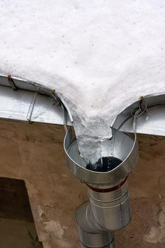 Melting ice and snow on the roof at the drainpipe. Vertical shot