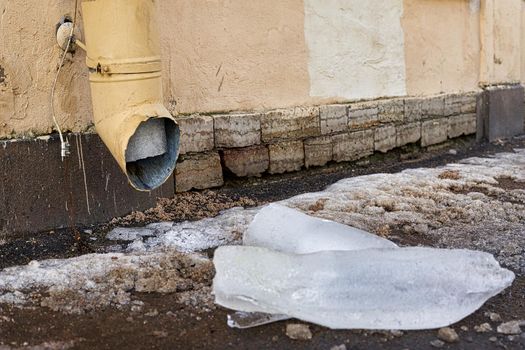 A large piece of ice dropped from the drainpipe lies on the street. Close up