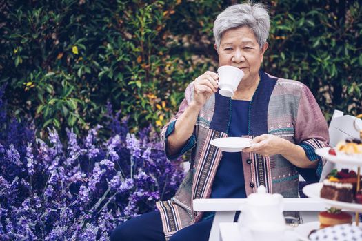 asian old elderly female elder woman drinking coffee tea in lavender flower garden. senior leisure lifestyle