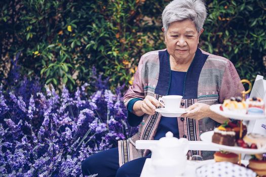 asian old elderly female elder woman drinking coffee tea in lavender flower garden. senior leisure lifestyle
