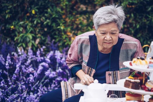 asian old elderly female elder woman resting relaxing in lavender flower garden. senior leisure lifestyle