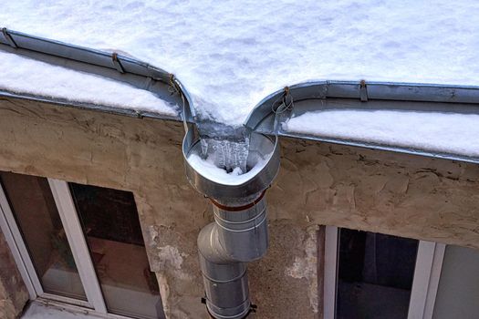 Fragment of the snow-covered roof of an old house with a drain with frozen water. Close up