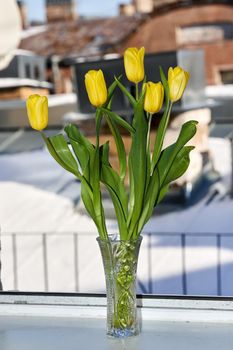 A bouquet of yellow tulips in a crystal vase on a windowsill. Vertical frame against the view from the window