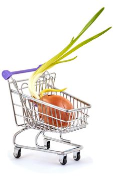 Onion with green feathers lies in a small supermarket trolley on a white background, close up