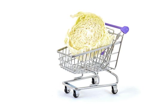 Green cabbage lies in a small supermarket trolley on a white background, close up