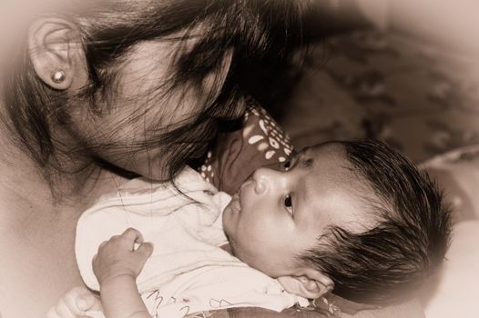 Adorable Mom and lulling newborn baby son. Loving portrait of happy mum hugging infant child on hands. Young Mother and little baby emotional attachment on Maternity Leave at home. Good morning.