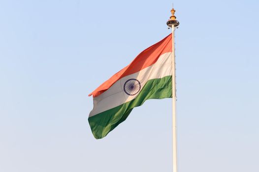 Indian flag flying against blue sky background. The National Flag of India is a horizontal rectangular tricolor (saffron, white and green color) with the Ashoka Chakra at its center.