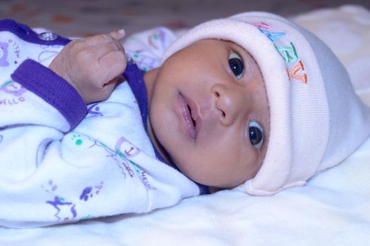 Close up portrait of a cute newborn baby boy lying bed and looking at camera. One month old Sweet infant toddler in winter clothing Closeup. Indian ethnicity. Front face. Child care background