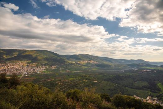 A view of a mountain range and a green valley in the morning at sunrise, against a dramatic backdrop of blue skies and clouds. North District Israel. High quality photo. Travel concept hiking