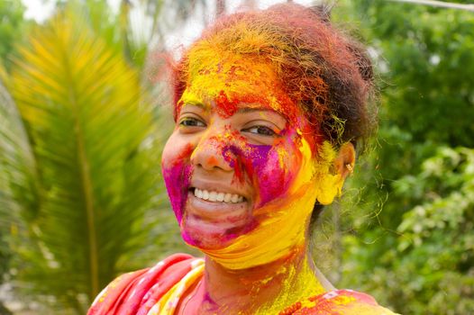 Portrait Of One Young Indian Happy woman with pink, yellow and red Holi colored powder paint on face During Holi Color festival. Front View. Looking at camera.