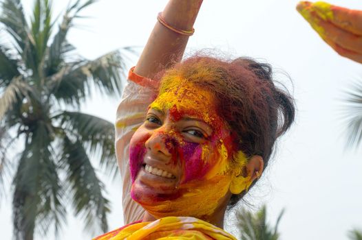 Portrait Of One Young Indian Happy woman with pink, yellow and red Holi colored powder paint on face During Holi Color festival. Front View. Looking at camera.