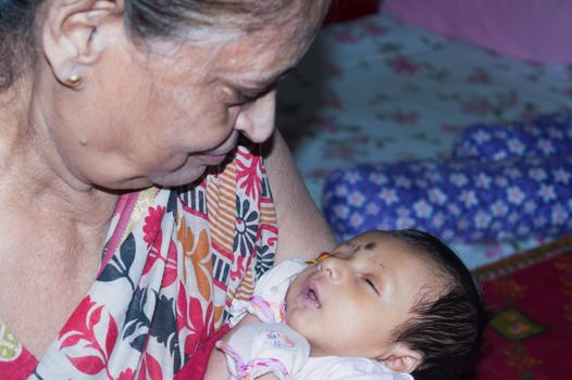 Newborn Little baby boy falling asleep lying on his old grandmothers lap. Toddler great granddaughter sitting on her great-grandmother's lap. Closeup