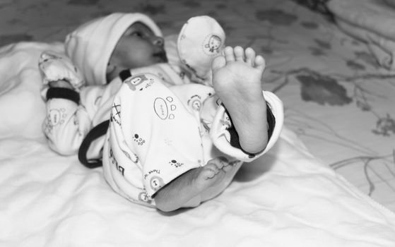 Closeup image of cute beautiful adorable baby boy foot posing on playing mood in winter clothing lying of bed on white blanket. One month old Sweet toddler. Front View. Childhood background.