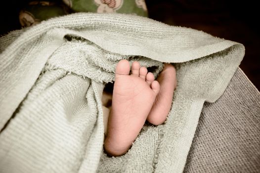 Newborn baby feet close up. The legs of a new born infant kid on a soft baby fur blanket. Cute love cozy background. Vintage color image. Copy space.