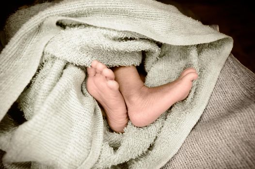 Newborn baby feet close up. The legs of a new born infant kid on a soft baby fur blanket. Cute love cozy background. Vintage color image. Copy space.