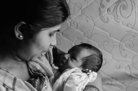 Close up face of a cute newborn baby boy making funny face in her mother lap. One month old Sweet little infant toddler. Indian ethnicity. Front view. Happy mother’s day background image.