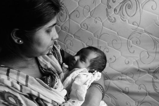 Close up face of a cute newborn baby boy happily looks at his mother in her mother lap. One month old Sweet little infant toddler. Indian ethnicity. Front view. Happy mother’s day background image.