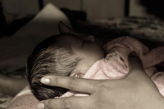 Beautiful Newborn baby boy Close up (6 days old) lying in mother lap in prenatal hospital. Kid wrapped in baby blanket (warm clothing) sleeping looking away. His mother consoling and resting her baby.